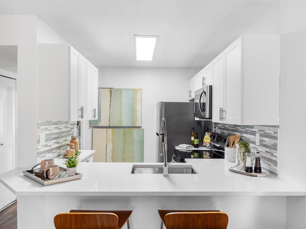 A modern kitchen with a white countertop and wooden chairs.